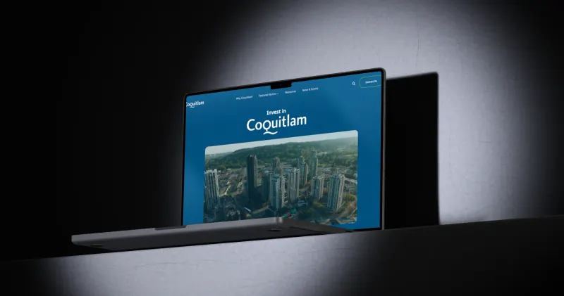 The Invest Coquitlam website we built, on a MacBook Pro under a spotlight