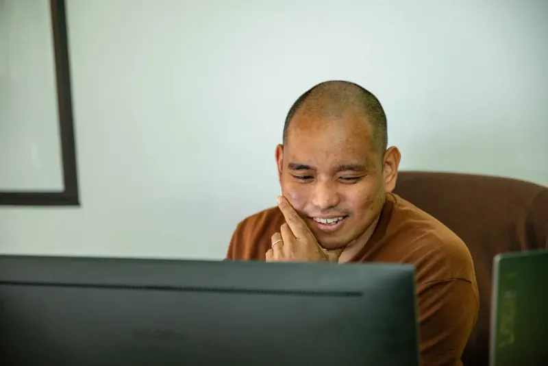 A man laughing at his monitor, chin resting on his hand