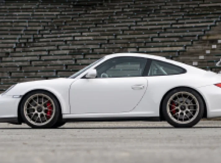 A white Porsche 911 in profile against a dark brick wall
