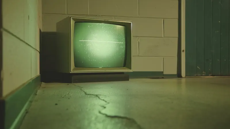 An old TV with a glowing green screen in a dim room with white brick walls.