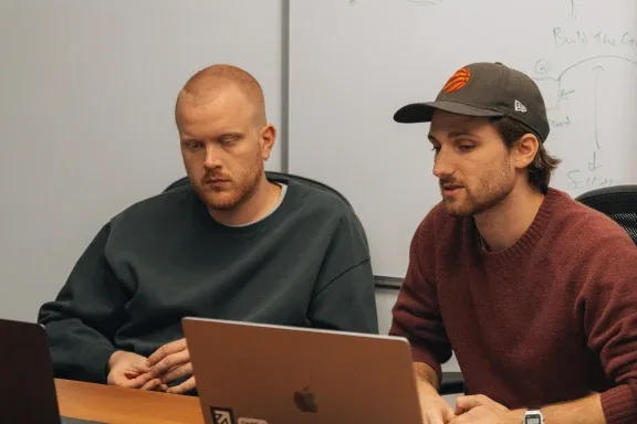 Two Setsail team members working at a laptop in front of a whiteboard