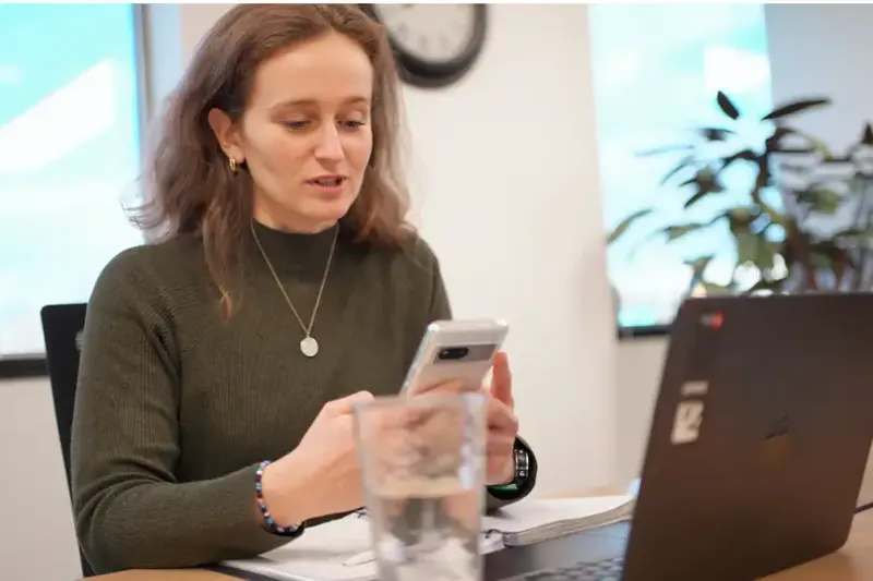 A woman reading her phone at her laptop