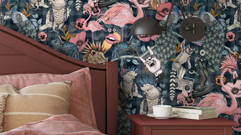 A bedroom papered in James Crossing’s Punk Rocks wallpaper, in denim blue, behind a red bed and bedside table
