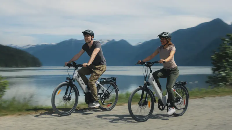 Two riders on EBGO e-bikes on a gravel path beside a lake, mountains behind, from our shoot