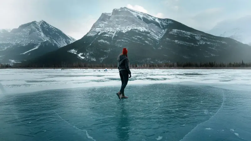 Woman in a red toque on a frozen turquoise lake facing snow-capped mountains, used in NH Staffing recruitment creative