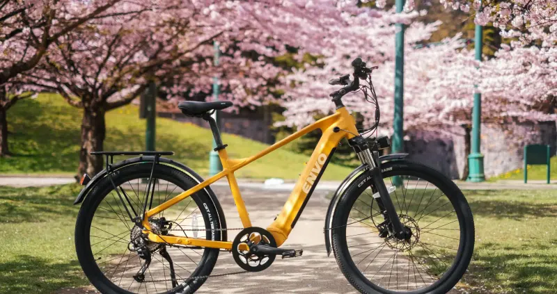 Yellow ENVO electric bike parked on a path under blossoming cherry trees