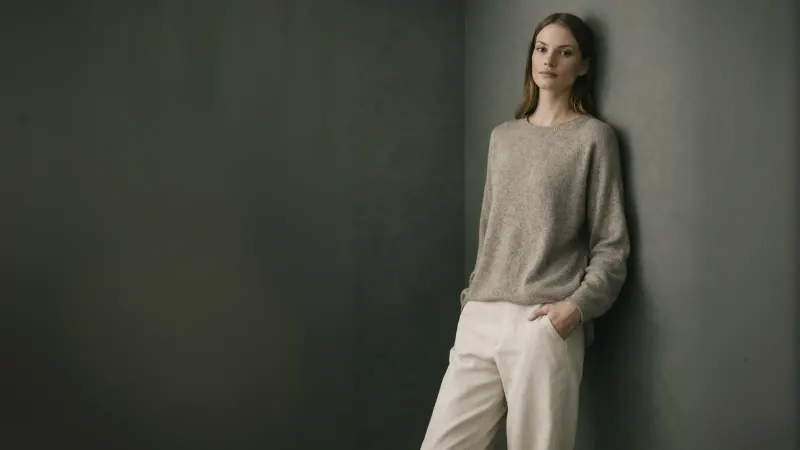 A woman in a soft knit sweater and cream trousers leaning on a dark wall, from the Pookie + Sebastian home page