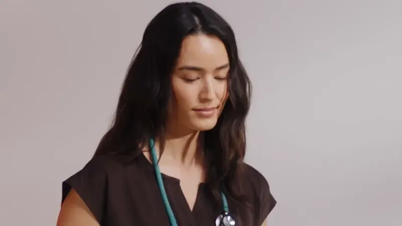 A nurse in dark Healing Hands scrubs with a stethoscope, from a Healing Hands EVRY ad