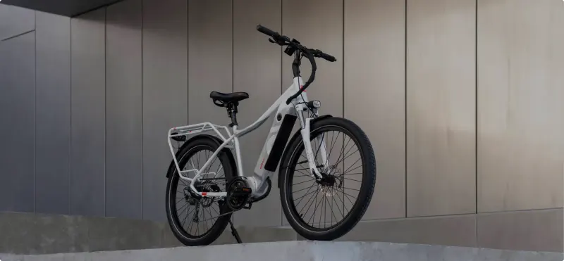 A white DŌST step-through e-bike parked against a grey panelled wall