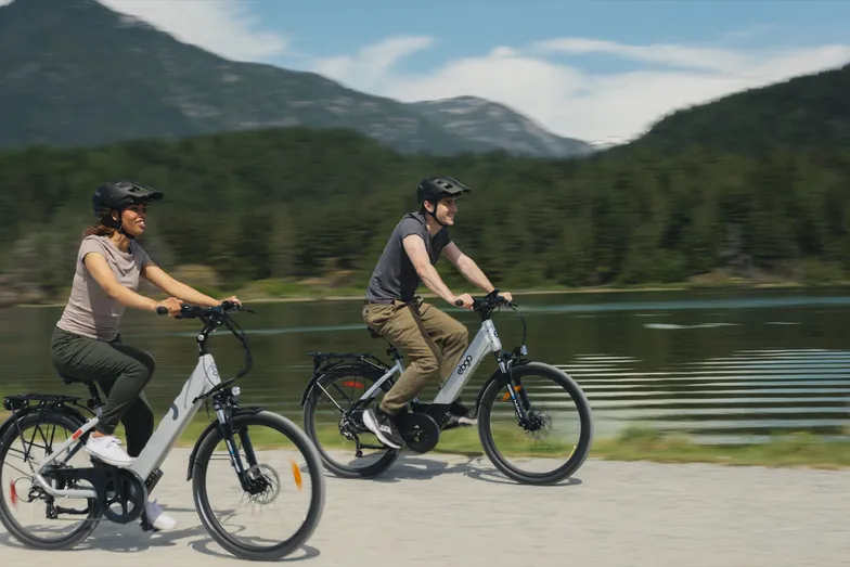 Two riders on EBGO e-bikes on a lakeside path below the mountains