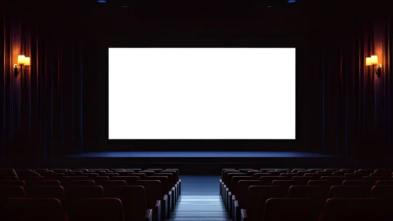 An empty cinema with red seats, glowing wall lamps and a blank white screen.