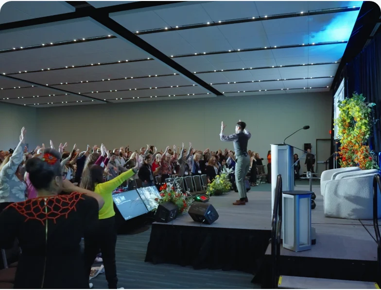 A packed conference hall at the Champions Retreat, the audience cheering a speaker on stage