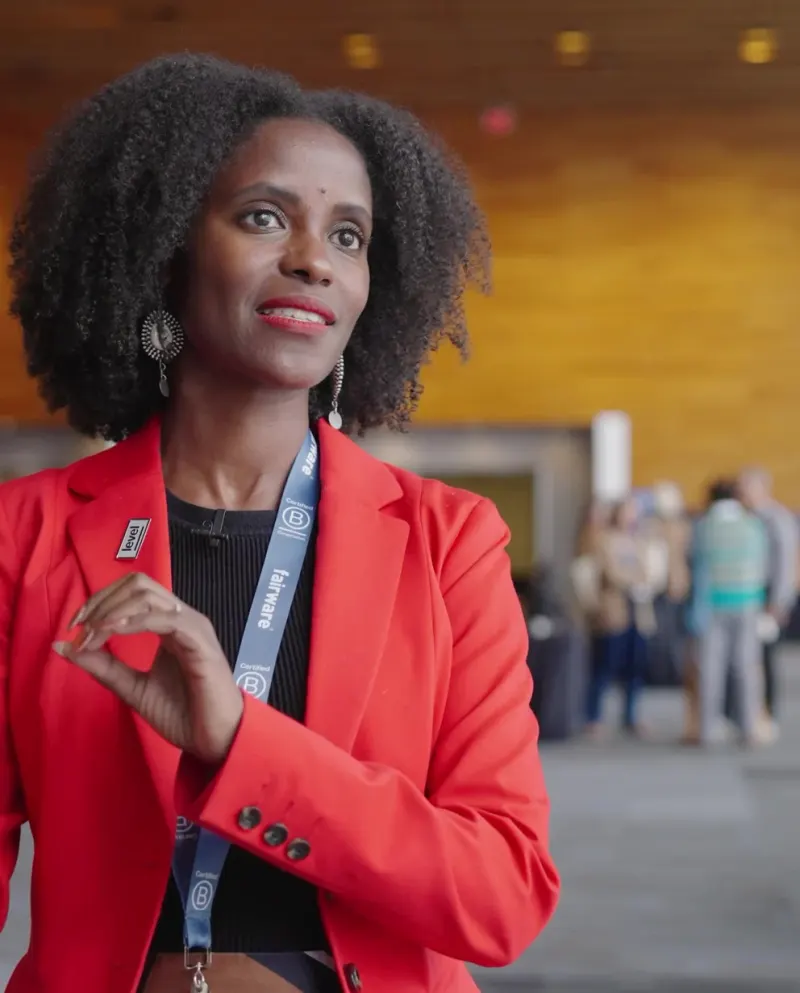 A speaker in a red blazer and a conference lanyard, mid-sentence at the Champions Retreat