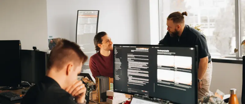 Three Setsail Marketing team members at a desk of monitors, talking through the work on screen