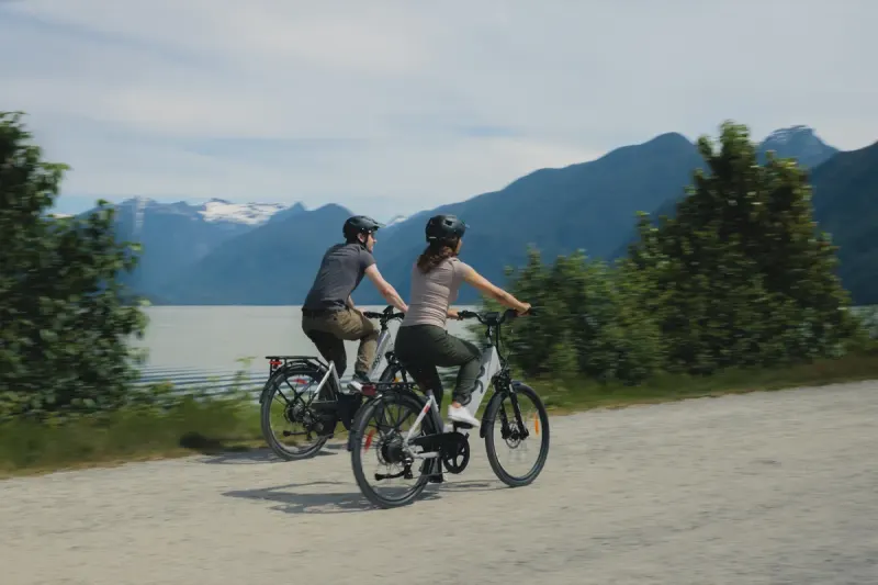 Two riders on EBGO e-bikes by a lake below snow-capped peaks