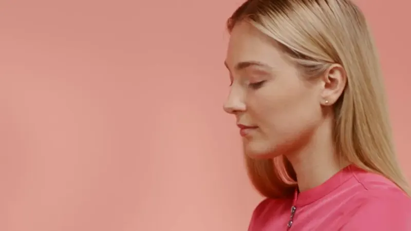 A nurse in pink Healing Hands EVRY scrubs, seated against a coral wall