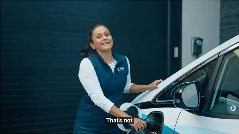 BC Hydro video still: a presenter in a BC Hydro vest plugging in an electric vehicle in front of a garage