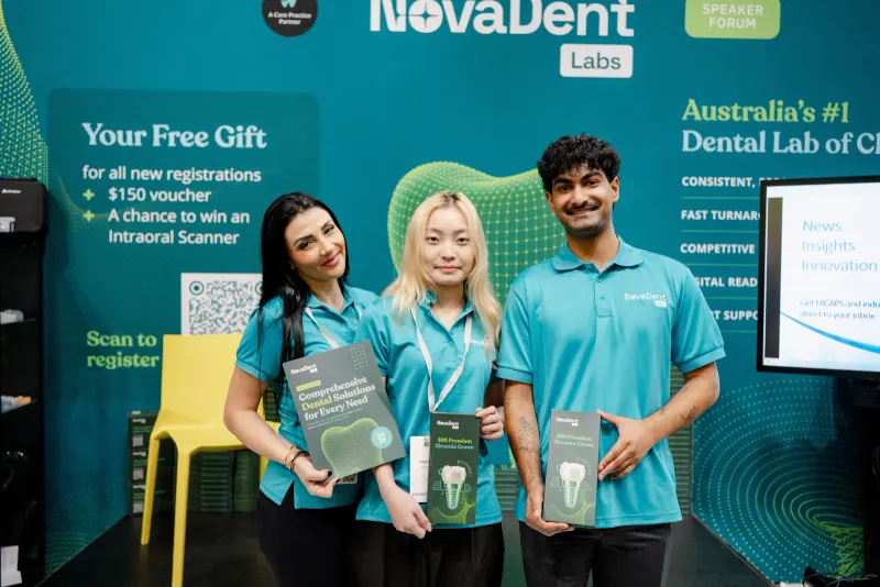 The NovaDent Labs team in teal branded polos at its trade show booth, holding brochures and product boxes