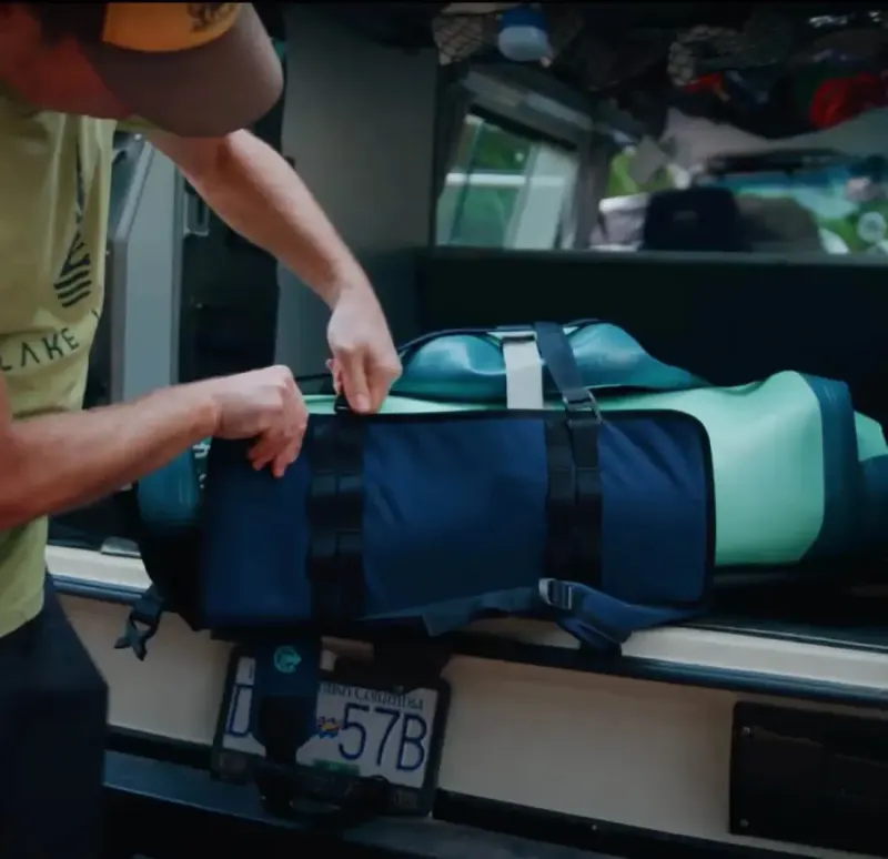 Person strapping a Squid Shoreline backpack and rolled paddleboard in the back of a vehicle