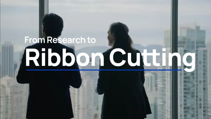 Two business leaders at an office window over Vancouver’s towers, under the title “From Research to Ribbon Cutting”