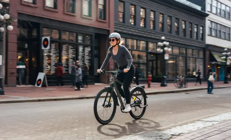 Woman in a helmet riding an ENVO electric bike along a brick street lined with heritage buildings