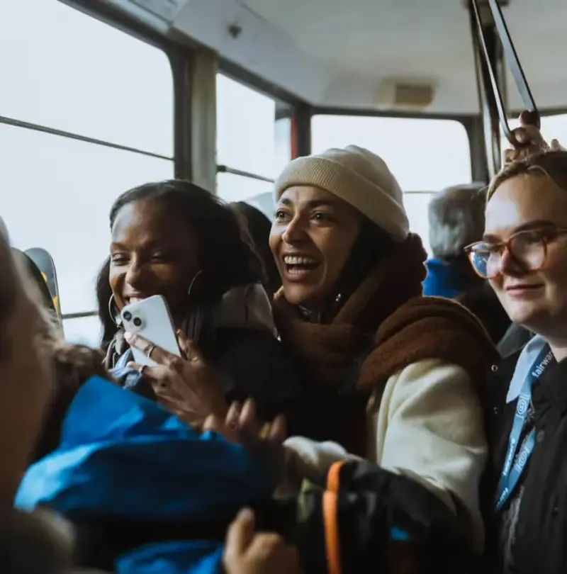 B Corp Champions Retreat 2024 attendees laughing together on a crowded shuttle, one holding up a phone