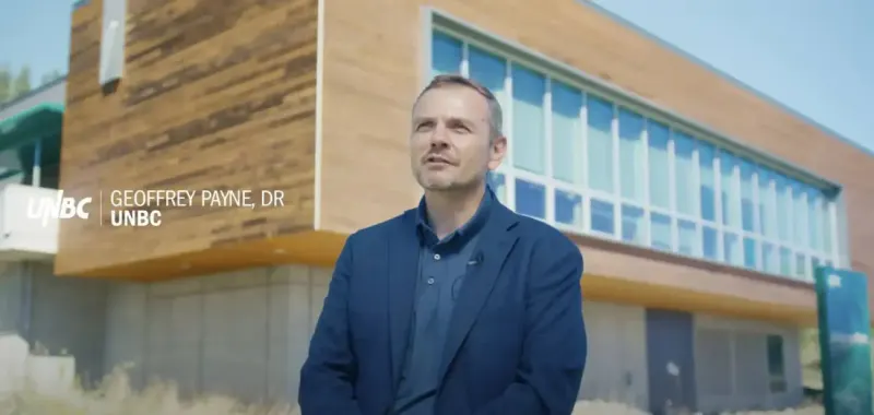 Video interview still for City of Prince George: researcher in front of a wood-clad building, captioned Geoffrey Payne, UNBC