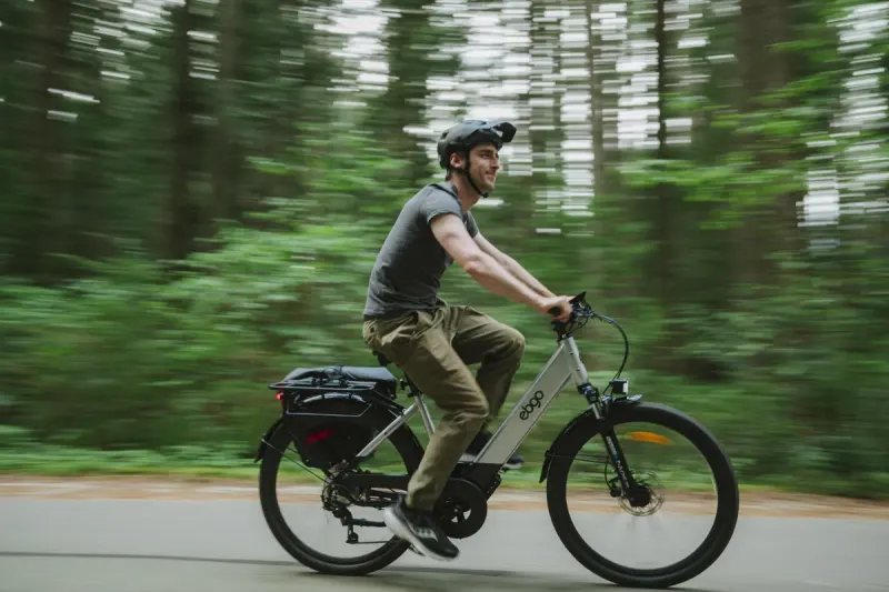 A rider on an EBGO e-bike on a paved forest road, the trees blurred with speed