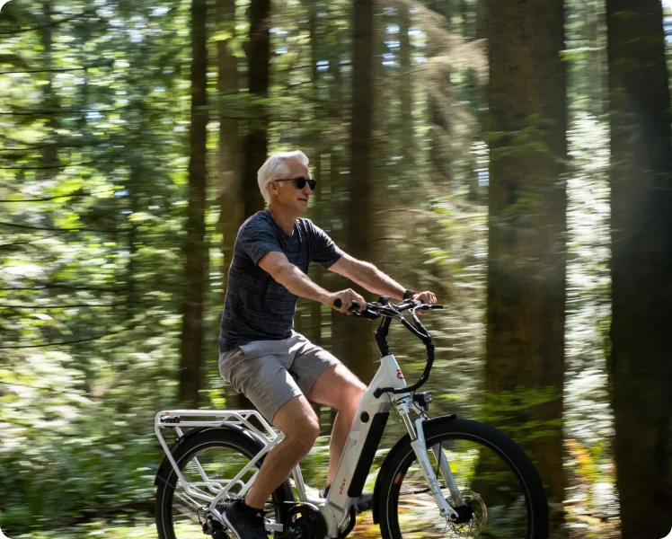 An older man riding a DŌST e-bike through a forest