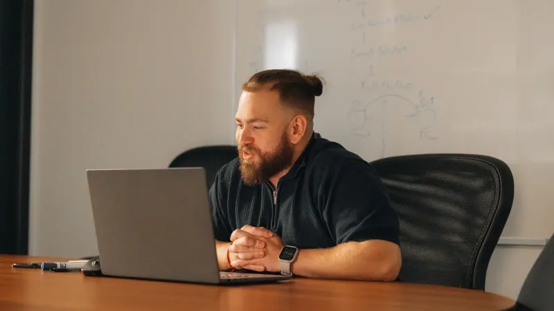 A Setsail strategist at a laptop in a meeting room, a whiteboard plan behind him.