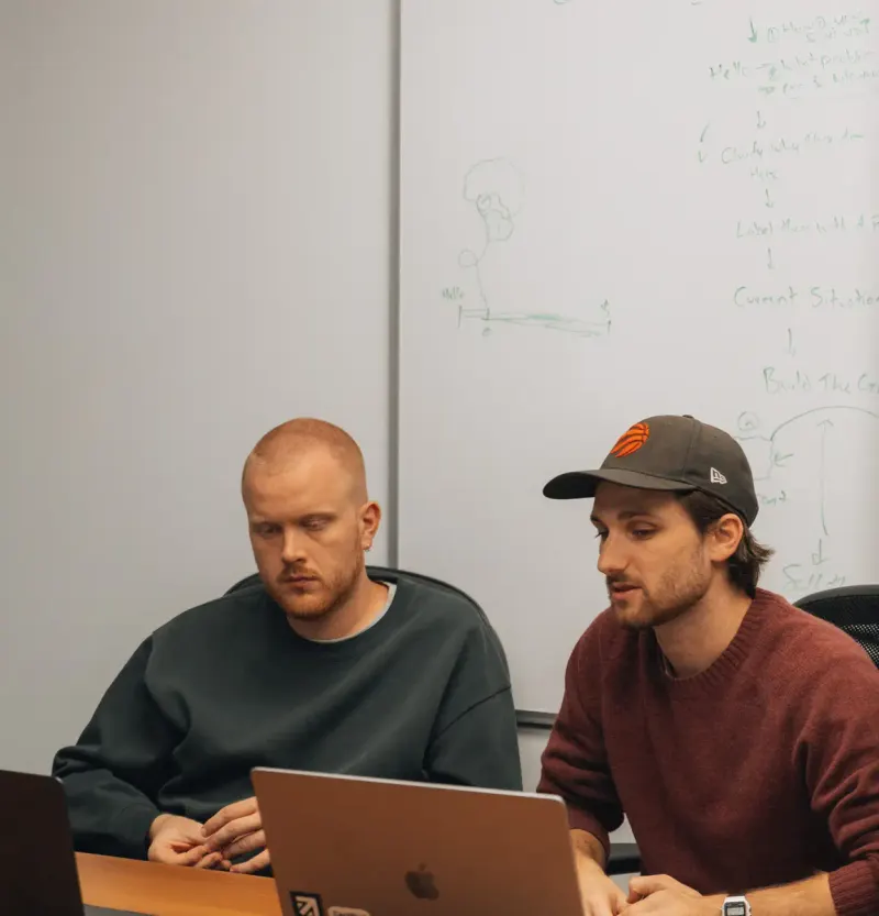 Two Setsail team members working at laptops in front of a whiteboard