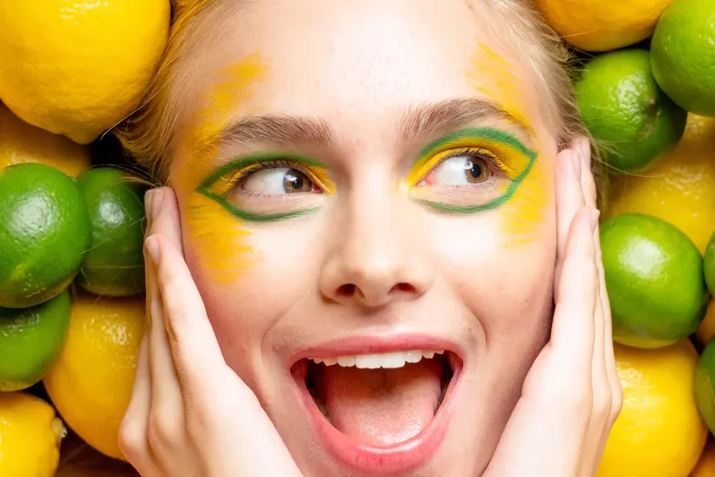 A laughing woman with yellow eye makeup, framed by limes and lemons