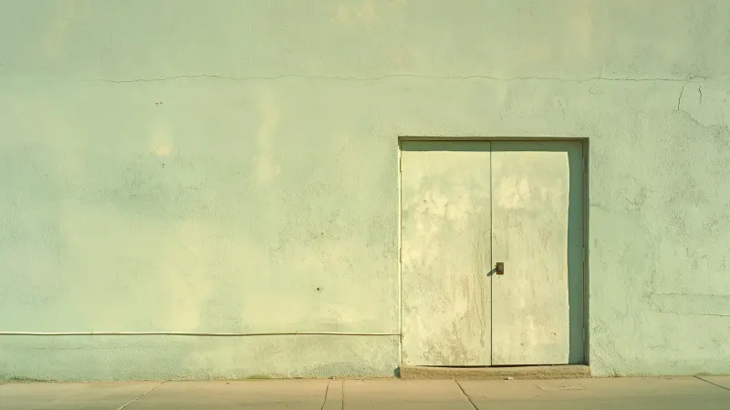 A pale green wall with a matching door above a concrete pavement.