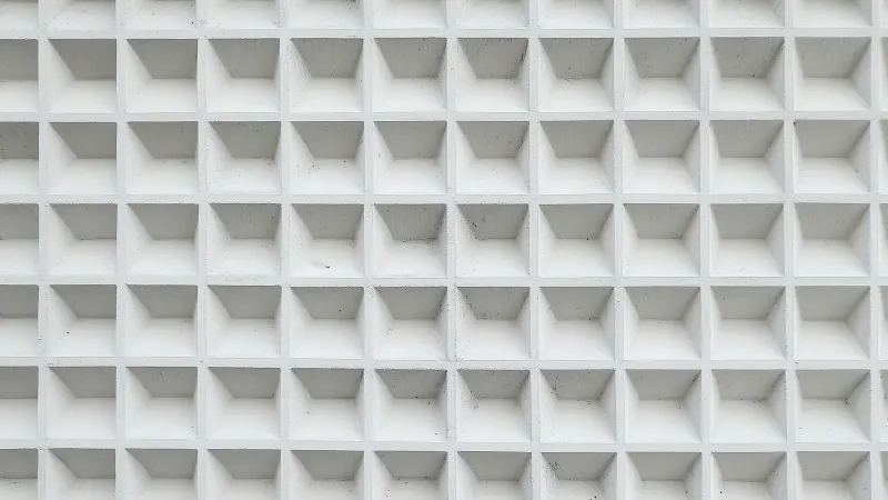 A light grey wall of identical recessed squares in a geometric grid.
