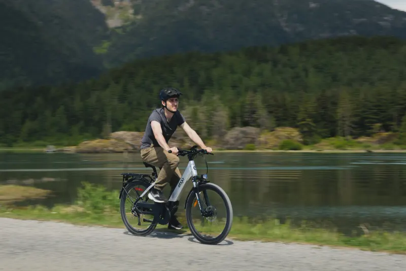 Two riders on EBGO e-bikes along a lakeside path with forested mountains behind