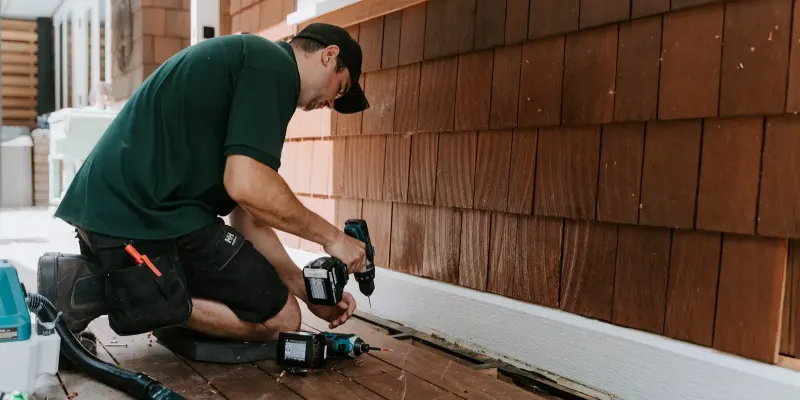 A Microworks technician repairing siding at the base of a cedar-shingle house