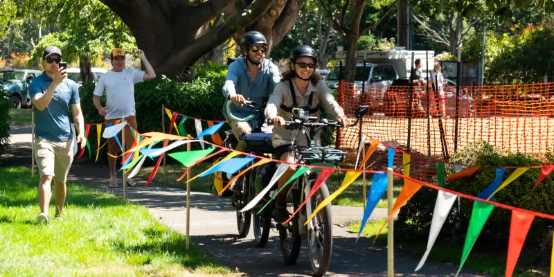 A group riding e-bikes along a path past strings of colourful bunting