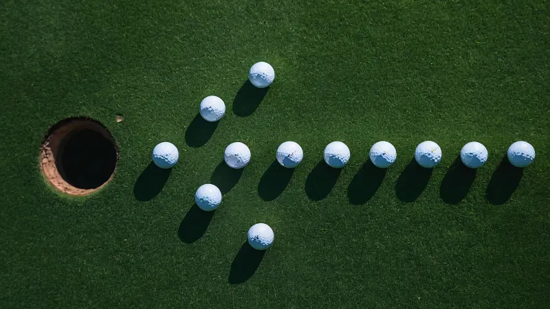 White golf balls laid out as an arrow pointing into a hole on a green.