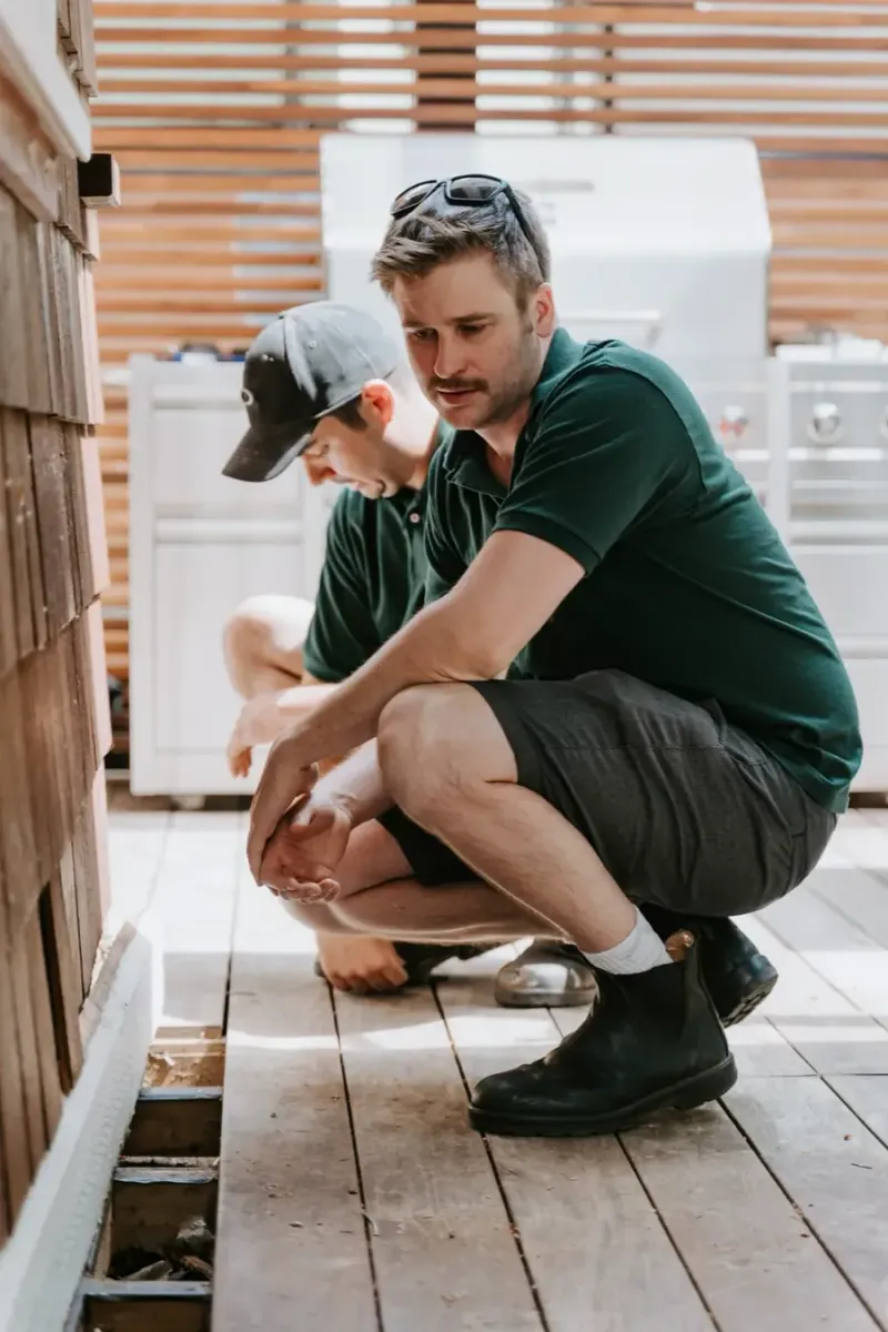 A Microworks technician crouched on a deck, checking a repair with a homeowner’s house behind him