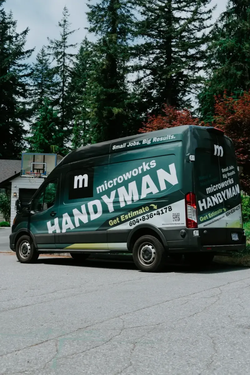 A Microworks Handyman van parked under tall evergreens, its side reading Small Jobs, Big Results
