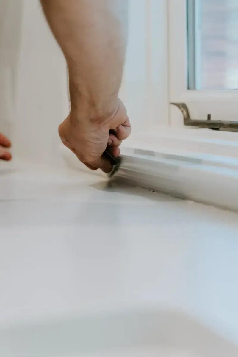 Close-up of a hand sealing the edge of a white window sill