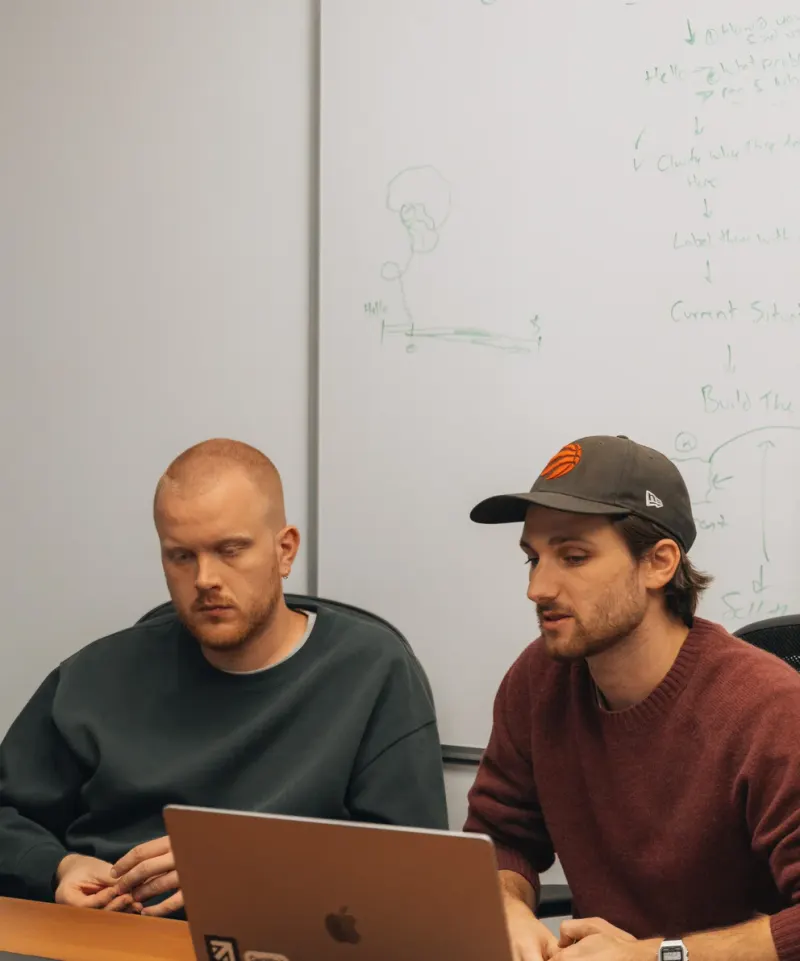 Two Setsail Marketing strategists working through a plan at a laptop, by a whiteboard