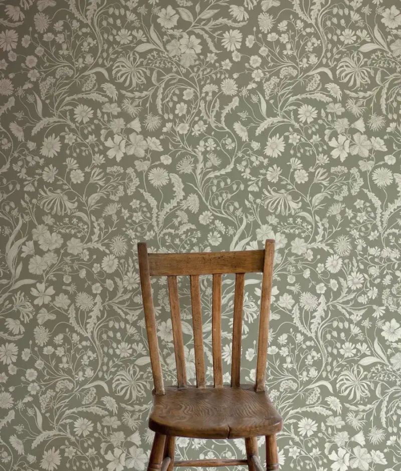 A wooden chair against Lost Garden wallpaper in a soft green