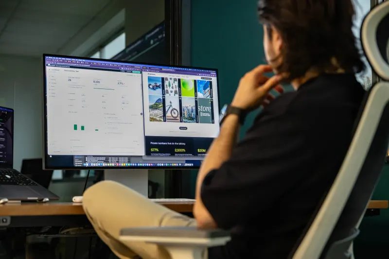 A Setsail team member, chin on hand, reviewing website and ad designs on a large monitor