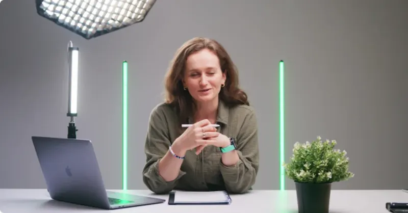 A presenter recording to camera at a desk under studio lights
