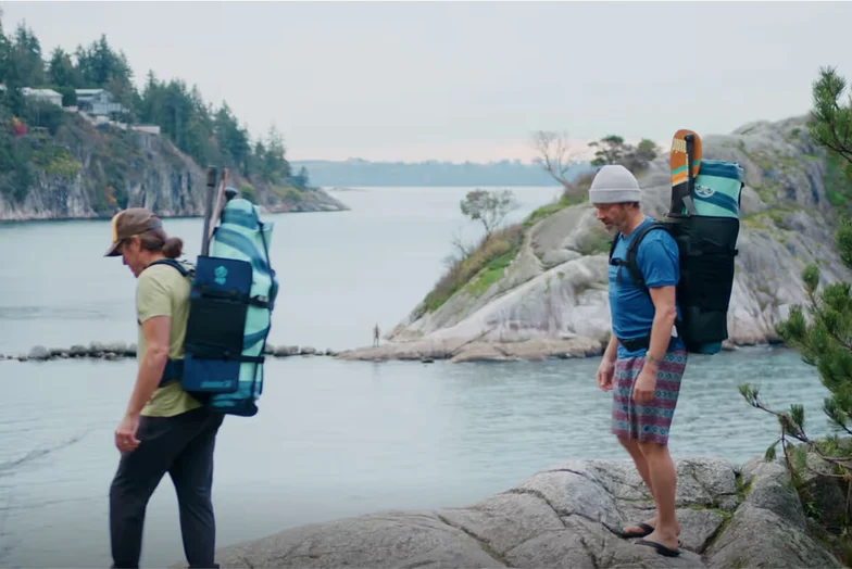 Two paddlers carrying Squid Paddle Co. packs along a rocky shoreline