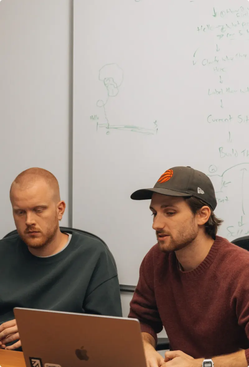 Two Setsail Marketing team members working through a plan on a laptop in front of a whiteboard