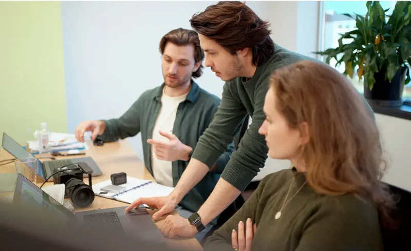 Three Setsail team members gathered around a laptop in an office, discussing the project