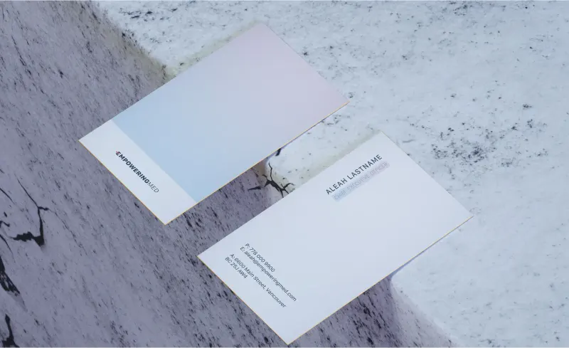 Two Empowering Med business cards on a marble surface, one with the logo and one with contact details