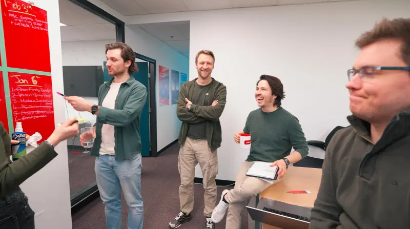 Steepe & Co project team laughing together beside a red whiteboard of dated task lists in the office